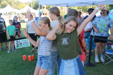A group of kids pose with peace signs at a festival game booth.