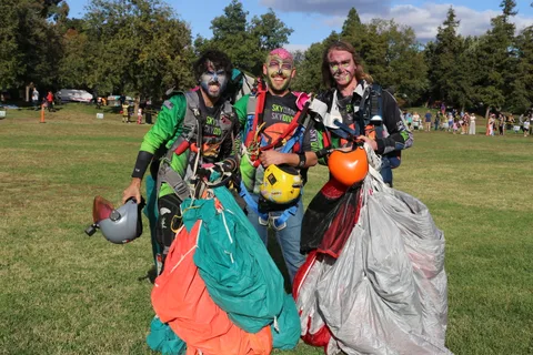 Costumed zombie skydivers pose together, one holding an orange helmet, after their landing.