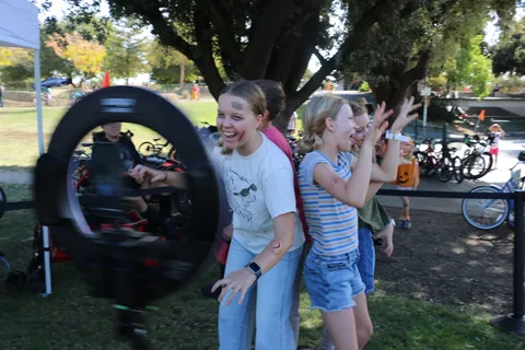 A blurred bike wheel spins beside two laughing festival-goers.