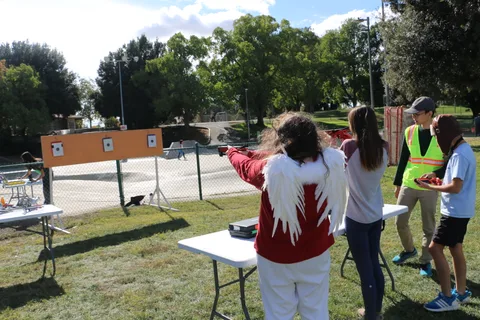 People gather near an archery-style booth set up in the park.