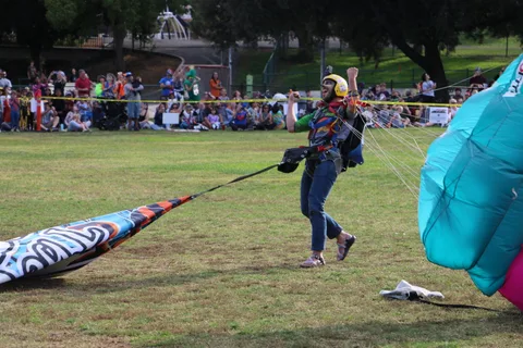 A skydiver pumps his fist and cheers after landing, a colorful banner trailing behind him.