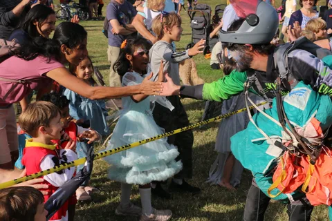 A girl in a tutu costume reaches to greet a costumed skydiver in the crowd.