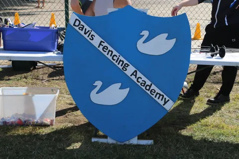 The Davis Fencing Academy sign stands near a fencing demonstration.