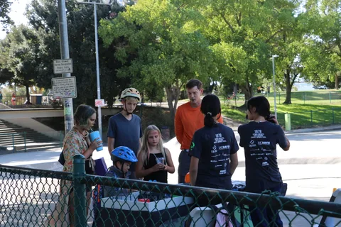 People walk with bikes along a path near the skate park.