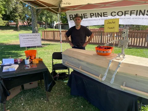 A vendor stands behind a wooden coffin display at the Blue Pine Coffins booth.