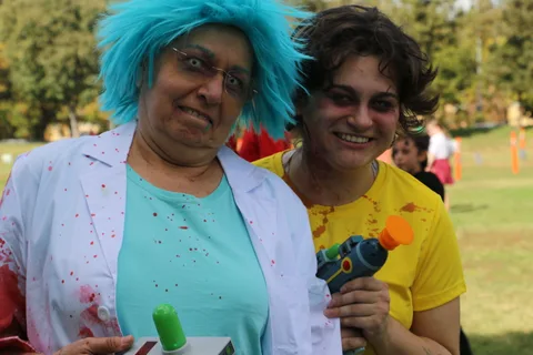 Two women in bloodied lab coat costumes make funny faces with toy guns.