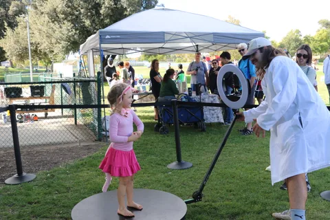 A young girl in pink stands on the photo booth platform near the tent.