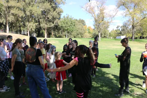 A group in zombie makeup and costumes gathers together on the grass.