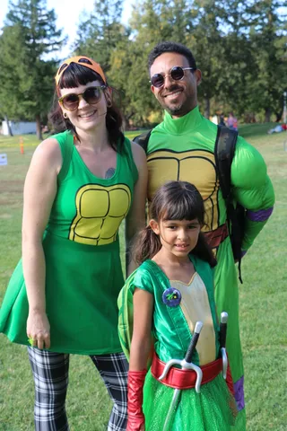 A family in matching Teenage Mutant Ninja Turtle costumes smiles together at the festival.