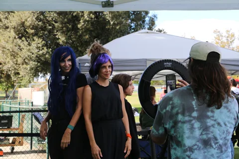 Two women in matching blue wigs smile together at the festival.