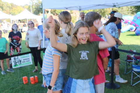 A group of kids raise their arms together near the bounce house.