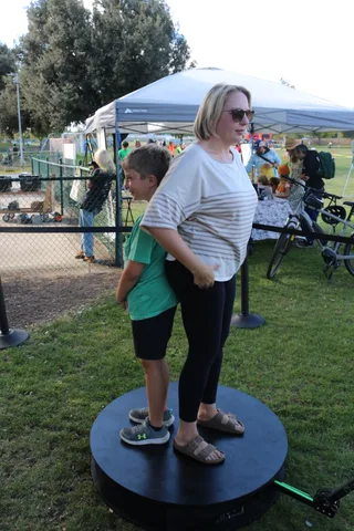 A woman in sunglasses walks past festival booths as a boy stands in the background.