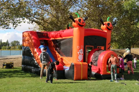 A pumpkin-themed inflatable bounce house draws a crowd of kids.
