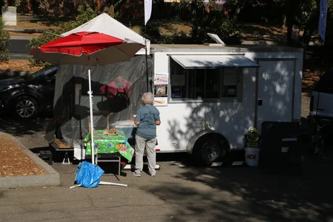 A food truck sits under a red umbrella at the festival grounds.