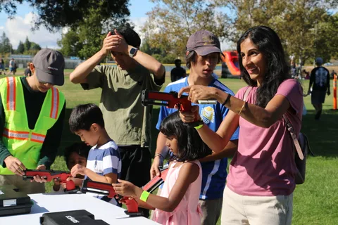 Children and adults react during a toy blaster activity at a booth.