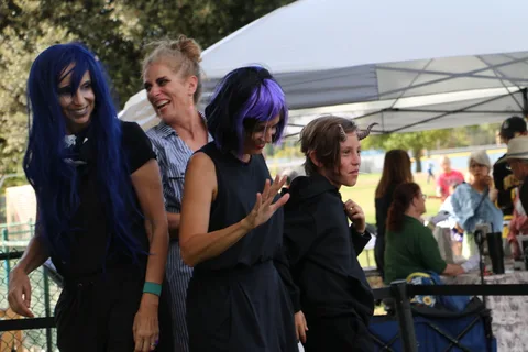 Festival-goers in blue wigs wave and smile for the camera.