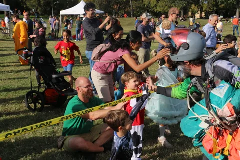 A crouching man and boy high-five a costumed skydiver in the crowd.