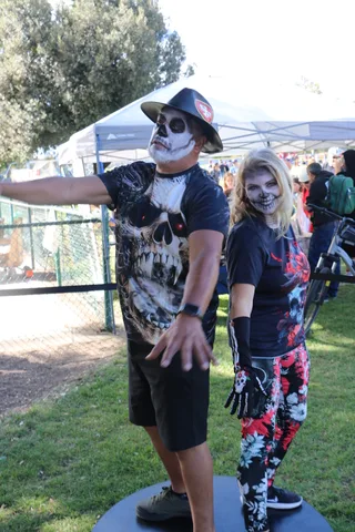 A man in skull makeup reaches out while a woman beside him laughs at the festival.