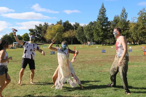 Three zombie-painted performers act out a scene together on the grass.