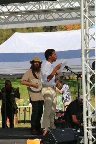 A speaker addresses the crowd from a stage with a plain white backdrop.