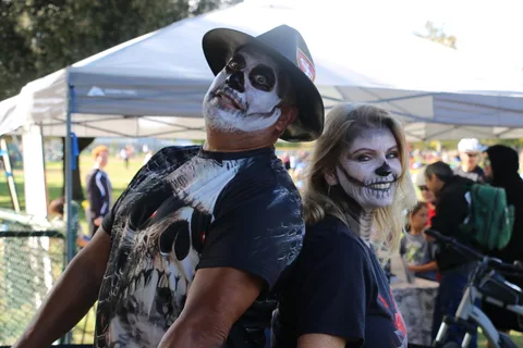 A man and woman in cowboy hats and skull face paint smile together at the festival.
