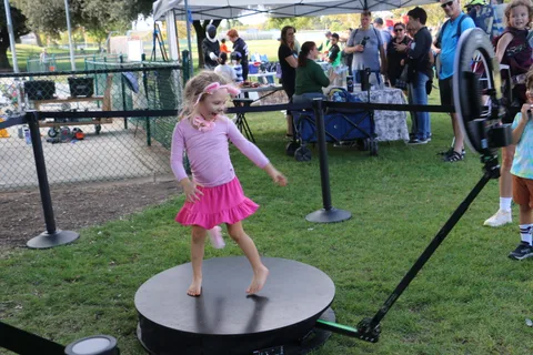 A young girl in a pink skirt dances joyfully on the photo booth platform.