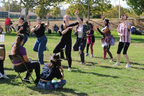 A costumed dance group performs a synchronized routine outdoors.