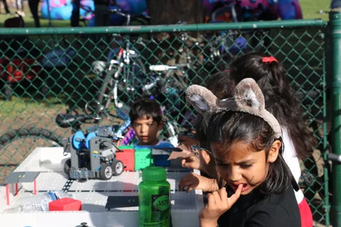 Two kids lean in to look at a robot on a table at a STEM booth.