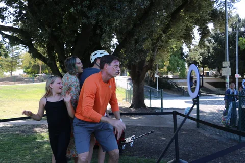 Teens in bike helmets sit and stand together near a fence.