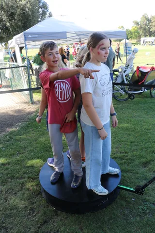 Two kids point and laugh together near a festival tent.