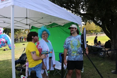 Costumed festival-goers pose in front of a green screen photo booth.