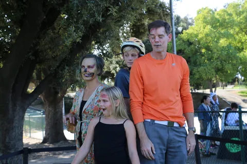 A family in zombie makeup and costumes poses together under the trees near the canal.