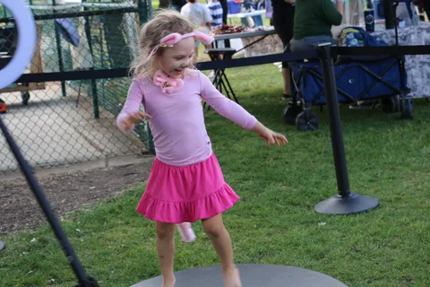 A girl in a pink skirt and ear headband runs along a fenced park path.
