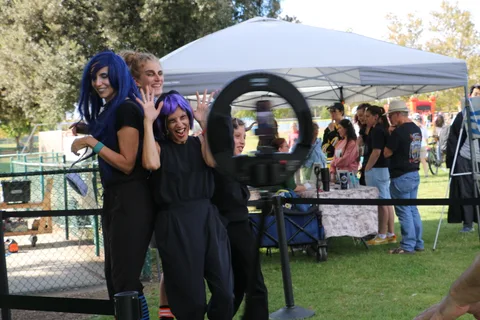 Women in wigs laugh together near the festival photo booth.