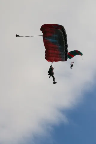 Two skydivers descend together under red parachutes against an overcast sky.