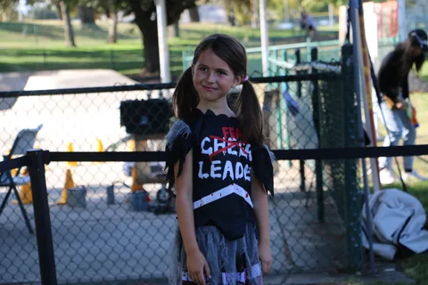 A girl in a cheerleader shirt stands near a portable photo booth light.