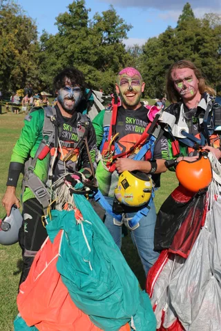 Three zombie-painted skydivers pose together with their gathered parachutes after landing.