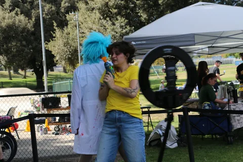 Two women in colorful wigs speak into microphones at the festival.