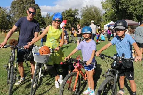 A family of four poses with their bikes, the mother in a bright wig and green costume dress.