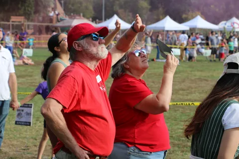 Two volunteers in red shirts point and cheer as they watch the skydivers overhead.