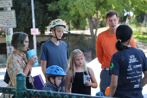 A group of teens wearing bike helmets gathers near the fence.
