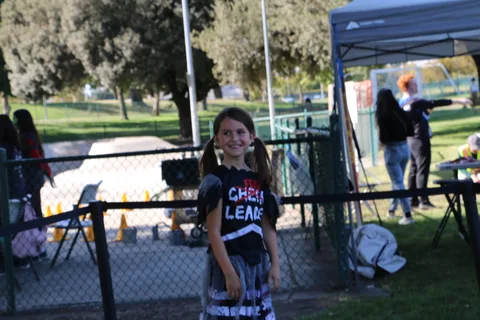 A girl in a cheerleader shirt stands beside the photo booth setup.