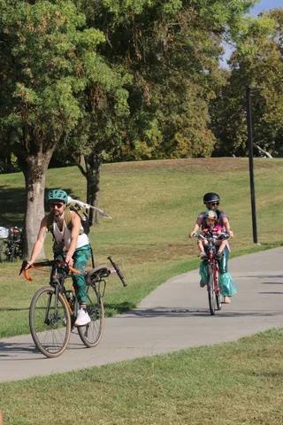 A rider in a green mermaid-tail costume pedals along the Davis bike loop path.