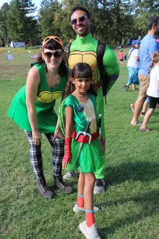A family in matching Ninja Turtle costumes poses together, smiling.