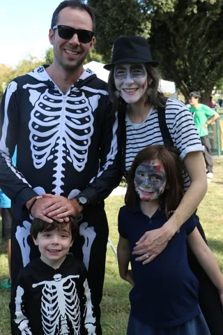 A family of four in matching skeleton costumes and zombie face paint smiles together outdoors.