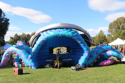 A DJ plays music from inside a giant inflatable octopus wearing oversized headphones.