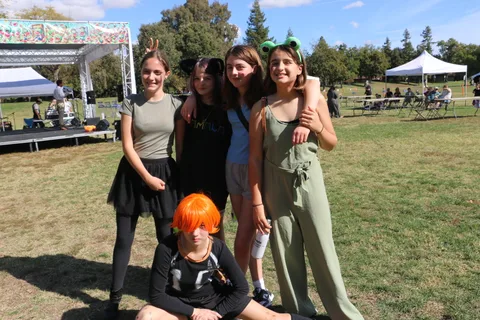A group poses together in the park, with a child in an orange wig in front.
