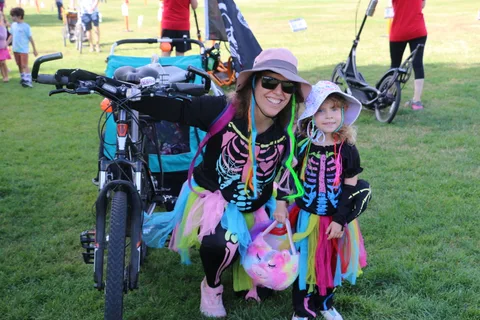 A woman and two children in colorful skeleton costumes pose together on a cargo bike.