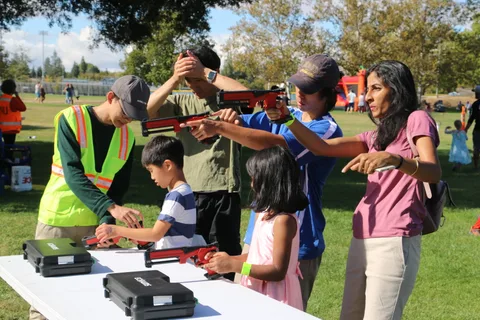 A group aims toy blasters together at a festival booth.