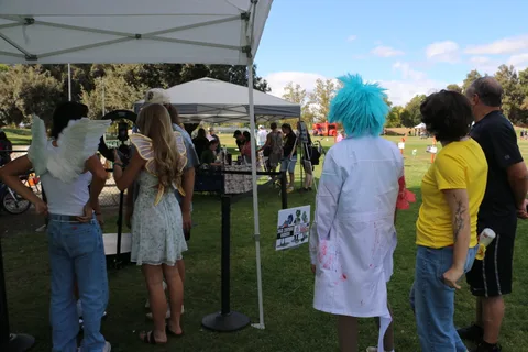 Two costumed festival-goers stand with their backs to the camera at a booth.